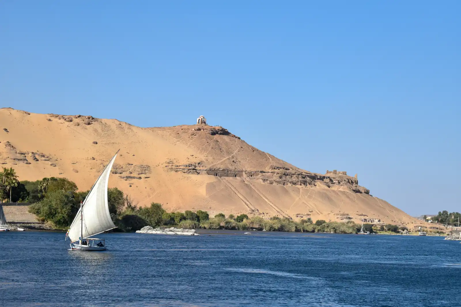 A tomb, a boat, water and mountains at Nile River in Luxor